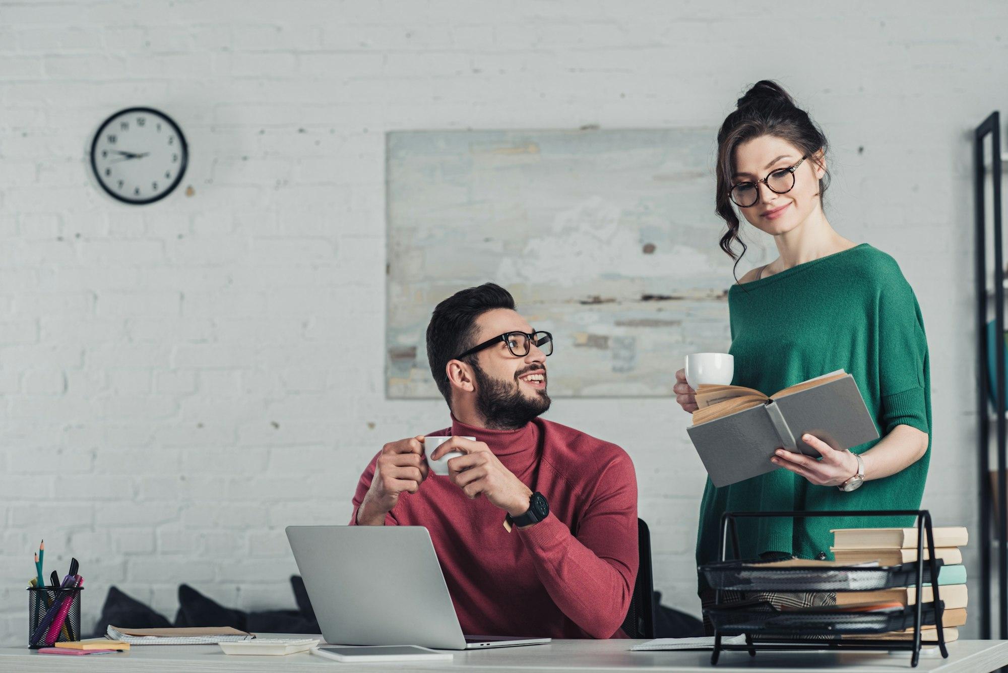 handsome bearded man looking woman studying with book in modern office