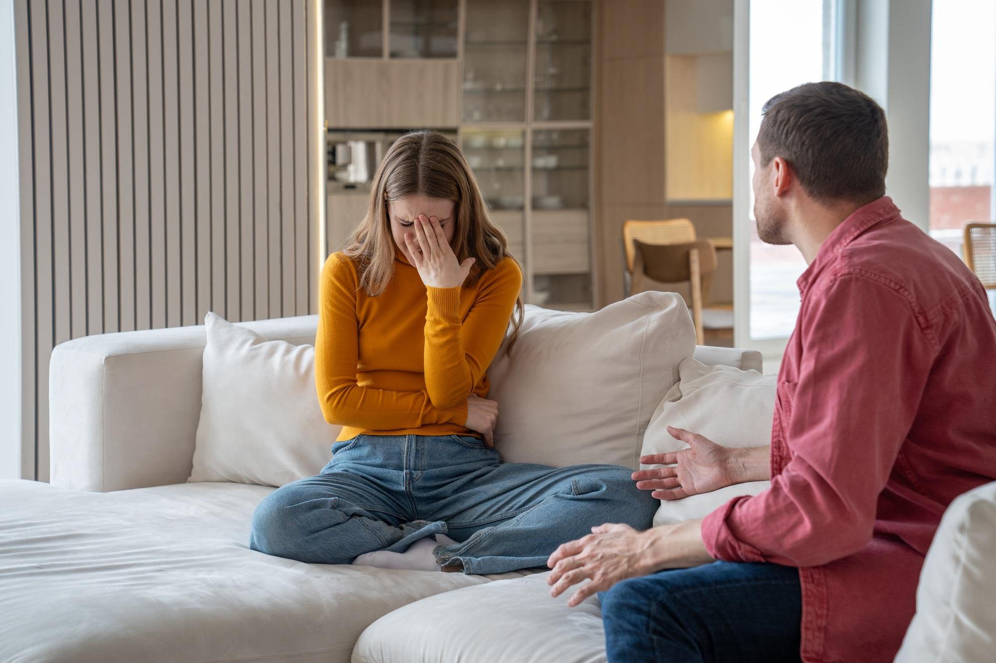 Unhappy upset woman crying discussing with cruel man husband in abusive relations sitting on couch.
