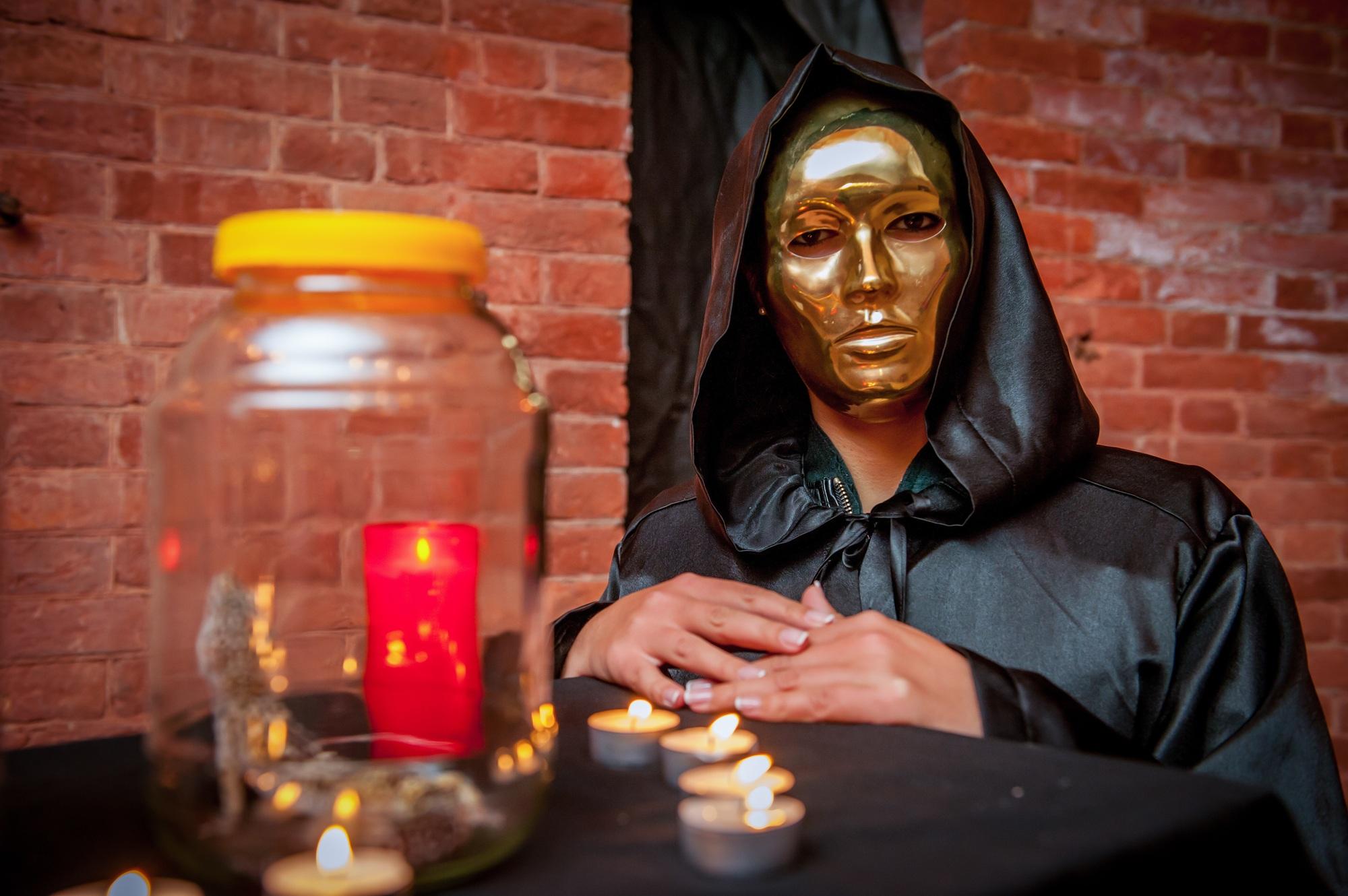 Closeup shot of a girl in golden mask and black hooded costume during a ceremony with candles