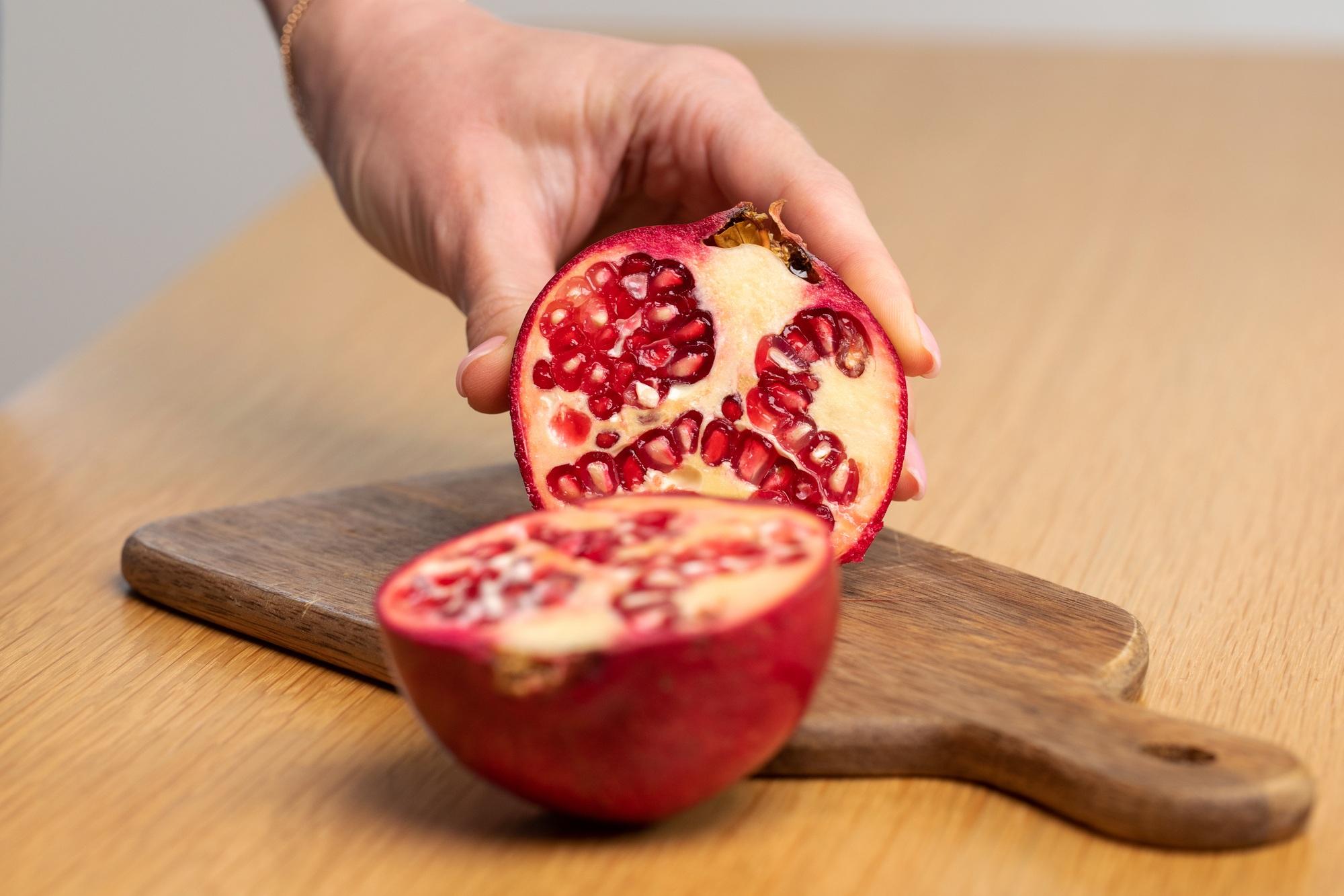 A woman bursts a grenade in close-up on a wooden table. Fruits.
