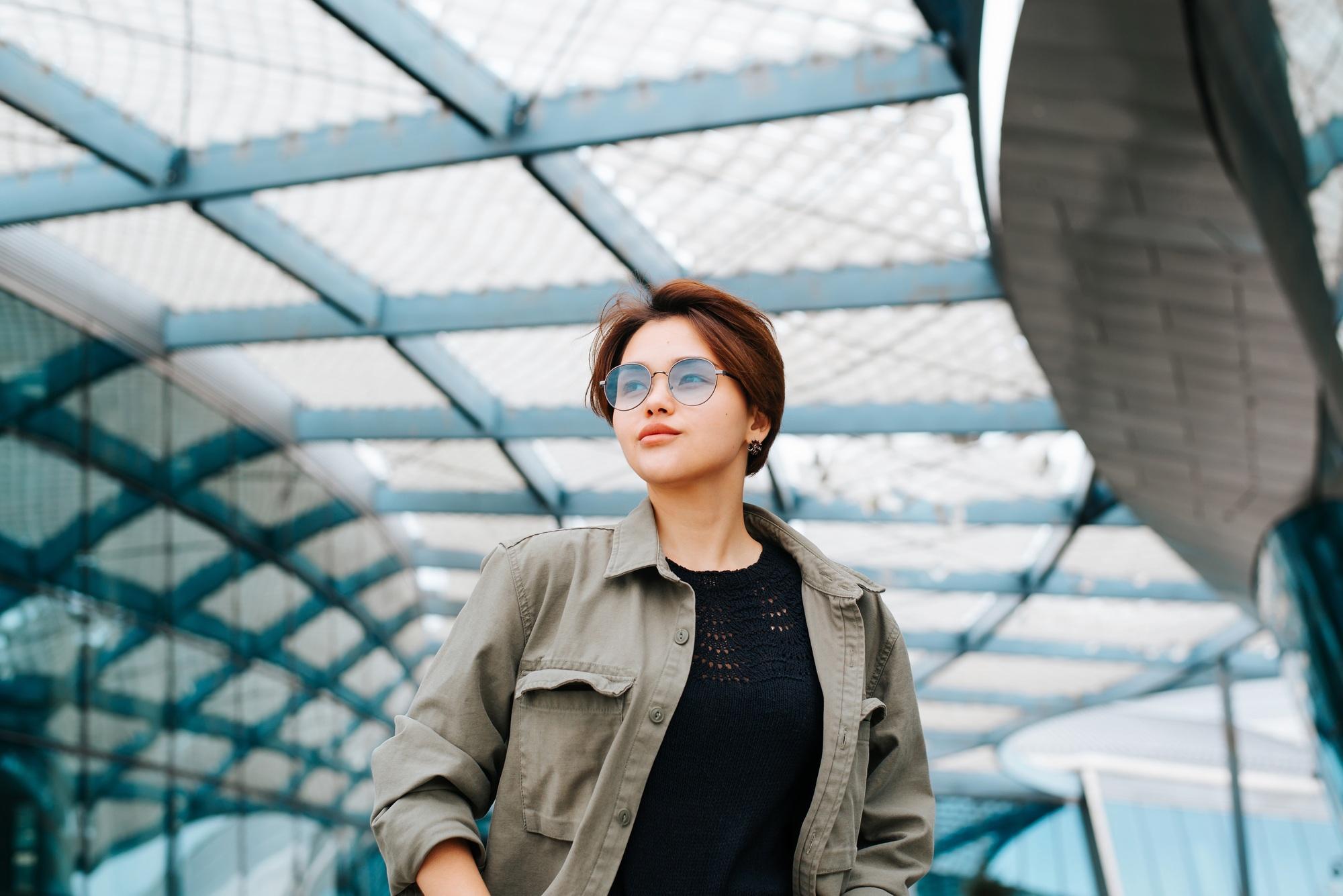 Fashionable young woman in fashion round glasses posing on background of modern architecture