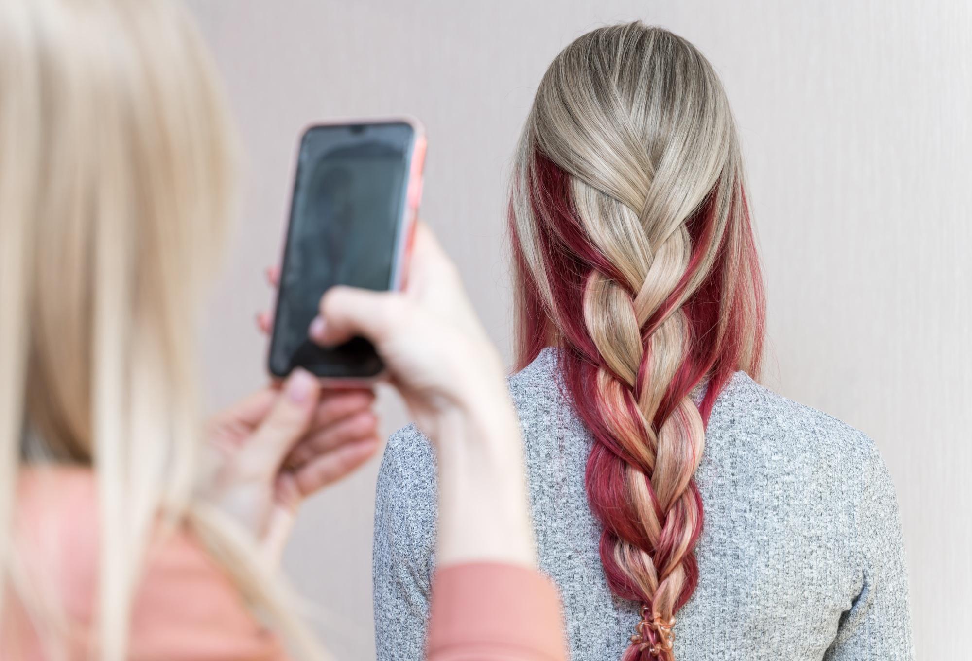 The hairdresser photographs the girl's hairstyle - long hair is braided in a multi-colored braid